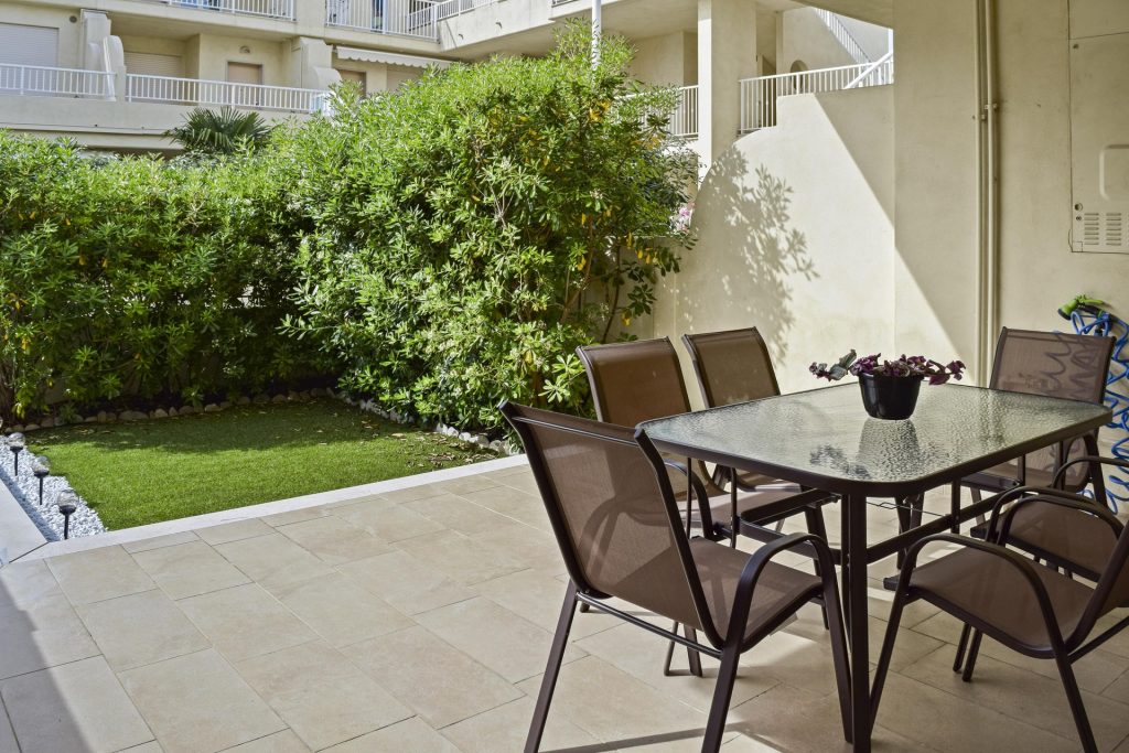 Giardino anteriore con tavolo in vetro e sedie, pavimentazione con erba sintetica e area relax.